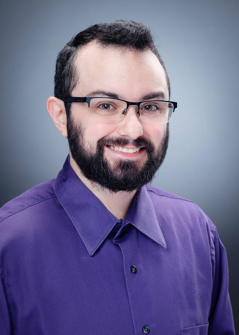 Headshot of Seth Levenson, a man with dark hair, a receding hairline and chinstrap beard, wearing glasses and a purple dress shirt, and smiling.